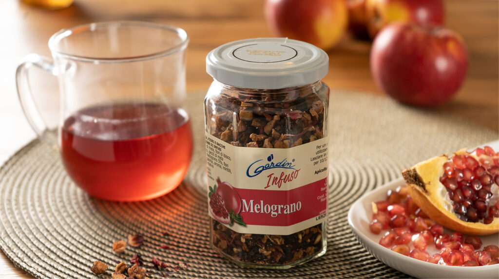 Infuso Melograno Apicoltura Gardin accanto a una tazza di infuso rosso, mele e melograno aperto