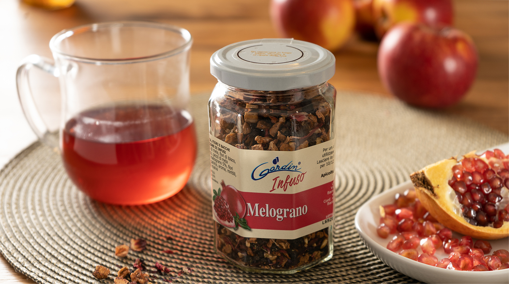 Infuso Melograno Apicoltura Gardin accanto a una tazza di infuso rosso, mele e melograno aperto